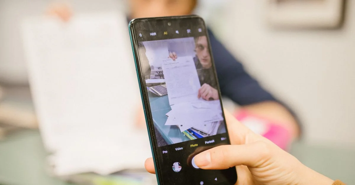Gros plan d'un étudiant utilisant un smartphone pour photographier des sujets d'examen dans une salle de classe.