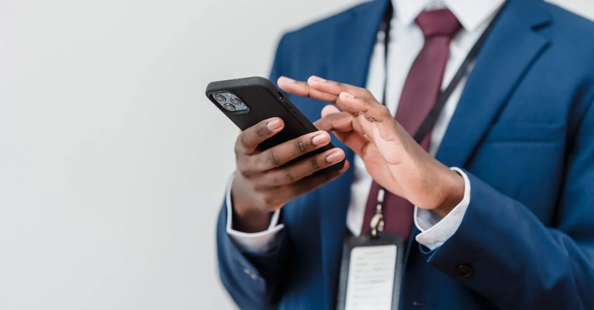 Un professionnel en costume utilisant un smartphone à l'intérieur, concentré sur l'interaction avec l'écran.