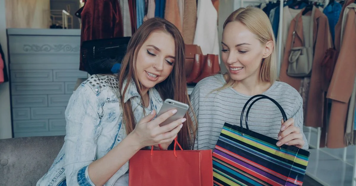 Deux femmes profitant de leurs achats ensemble, partageant du contenu sur un téléphone dans une boutique élégante.