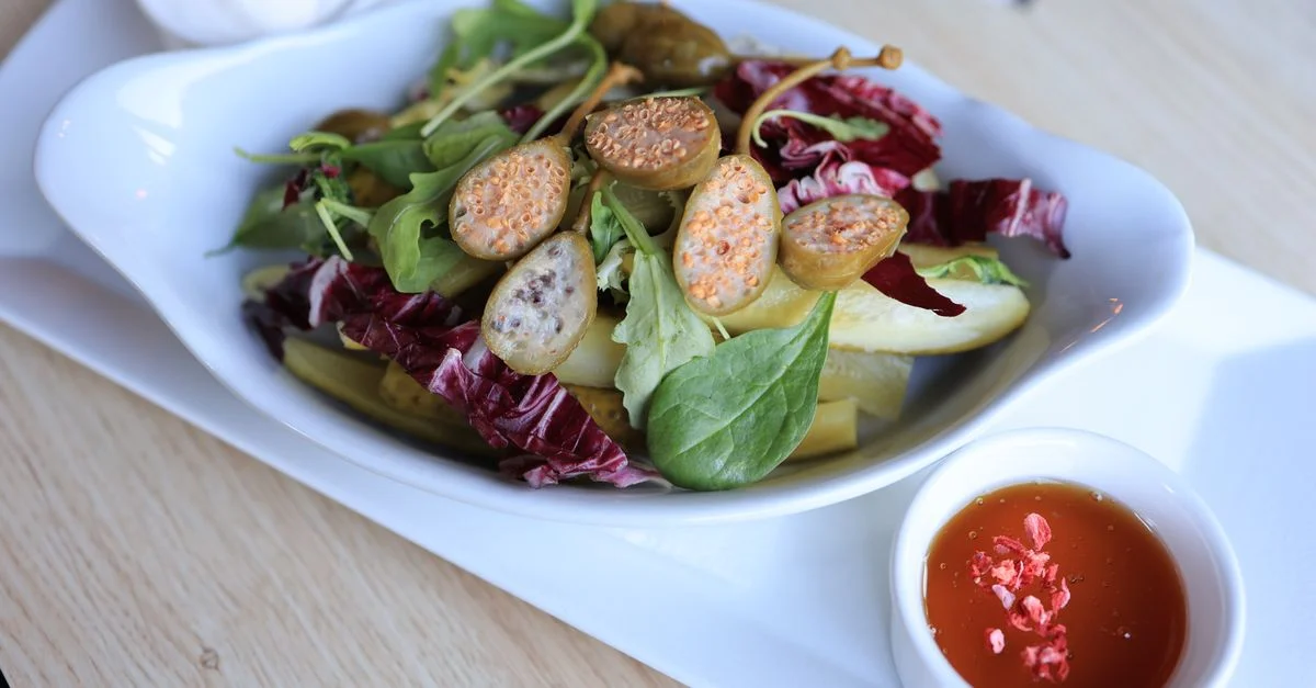 Salade mixte vibrante avec des légumes frais, des figues, des câpres et de la vinaigrette, servie dans un plat blanc.