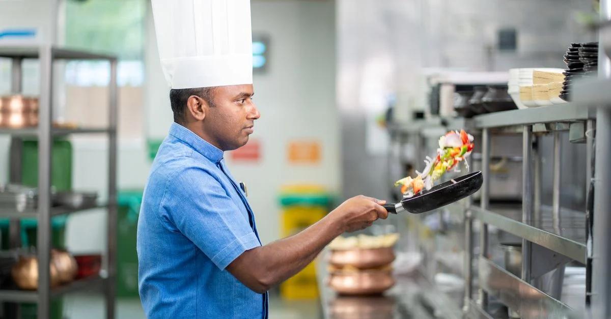 Chef professionnel lançant une poêle de légumes dans une cuisine commerciale, mettant en avant ses compétences culinaires.