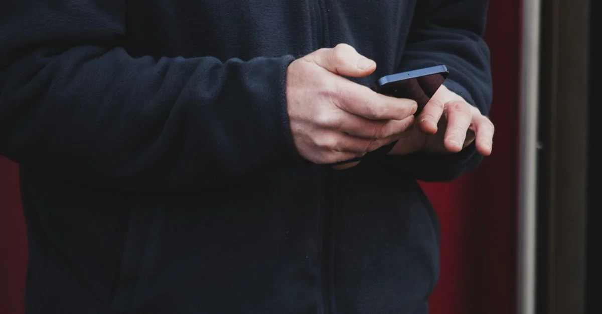 Gros plan sur une personne en train d'envoyer des SMS sur son smartphone à l'extérieur, à Dublin, portant une veste bleu marine.