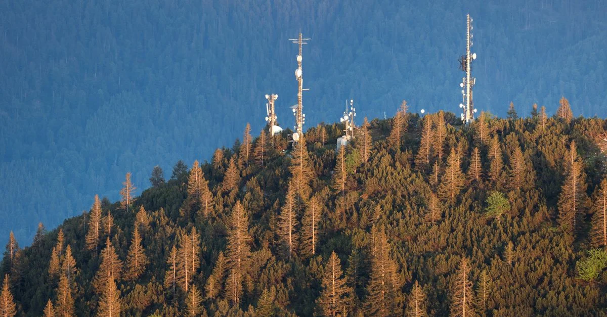 Un sommet de montagne serein avec des antennes radio entouré d'une dense forêt pendant le coucher du soleil.