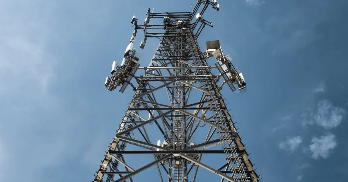 Un plan en contre-plongée d'une haute tour de communication en métal avec plusieurs antennes, sur fond de ciel bleu dégagé.