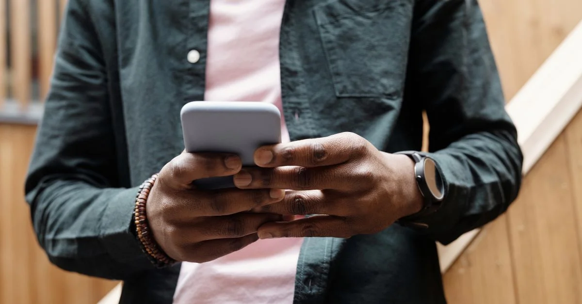 Gros plan sur un homme utilisant un smartphone, mettant l'accent sur les mains et l'appareil dans une atmosphère relaxante en intérieur.