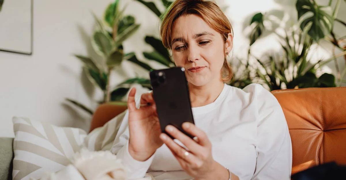 Femme adulte utilisant un smartphone sur un canapé confortable à la maison, entourée de plantes.