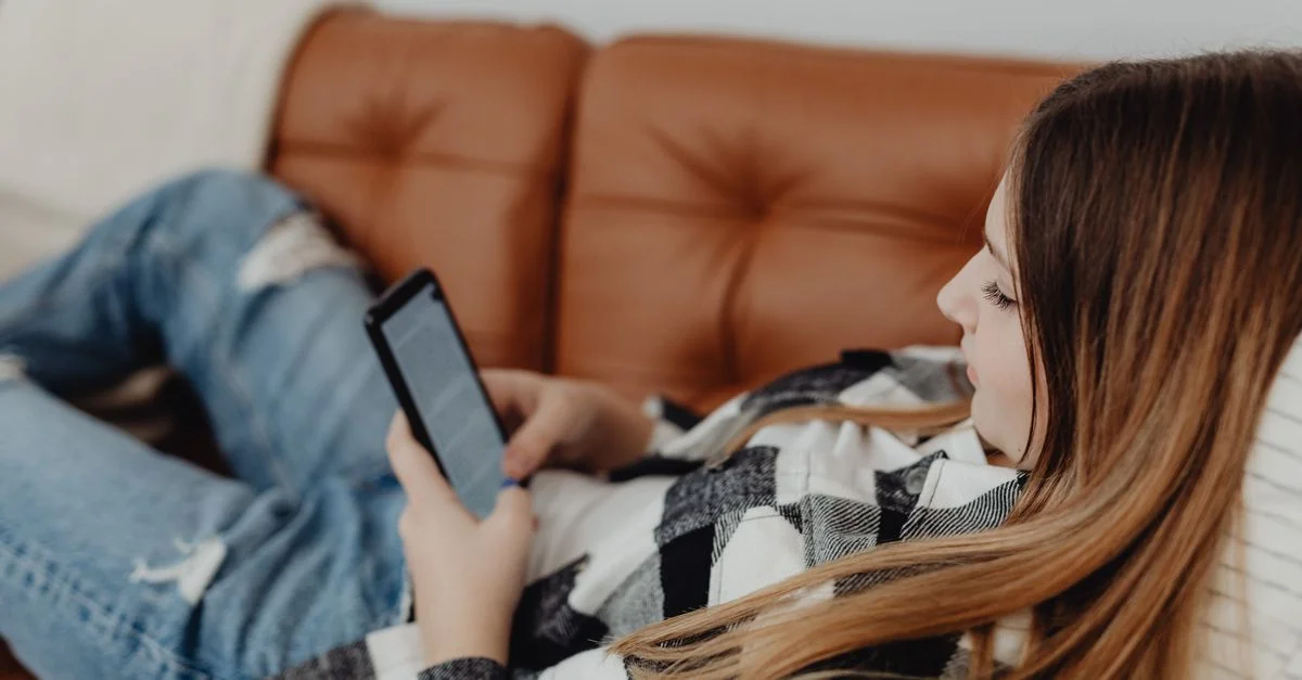 Femme allongée sur un canapé en cuir profitant d'un moment décontracté avec un smartphone.