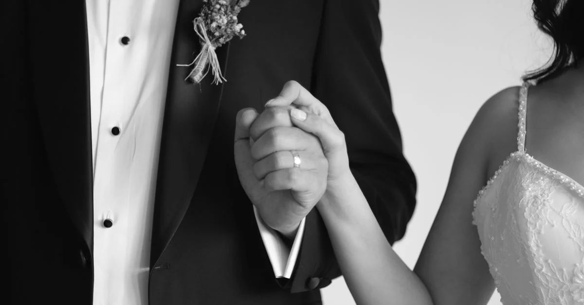 Gros plan en noir et blanc d'un couple de mariés se tenant par la main, symbole d'amour et d'engagement.