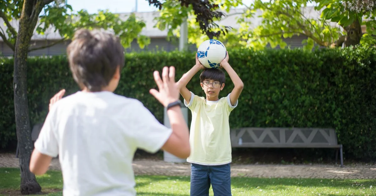 Deux jeunes garçons jouent avec un ballon de soccer dans un parc portugais ensoleillé, mettant en valeur le plaisir en plein air.