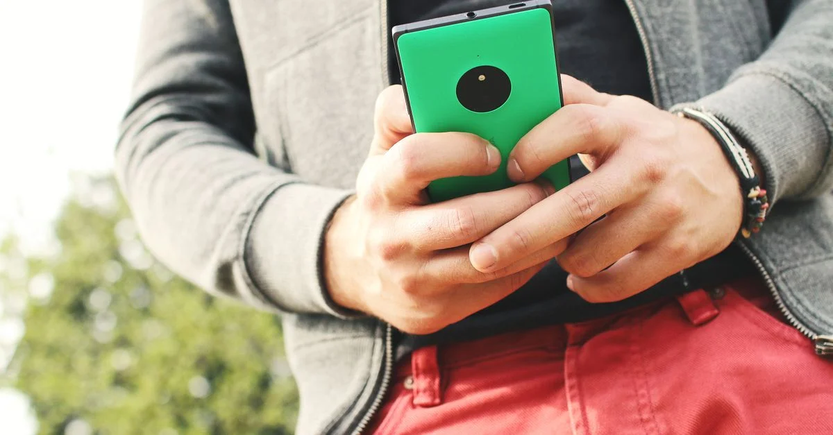 Une personne en vêtements décontractés à l'extérieur tenant un smartphone, soulignant un mode de vie connecté.