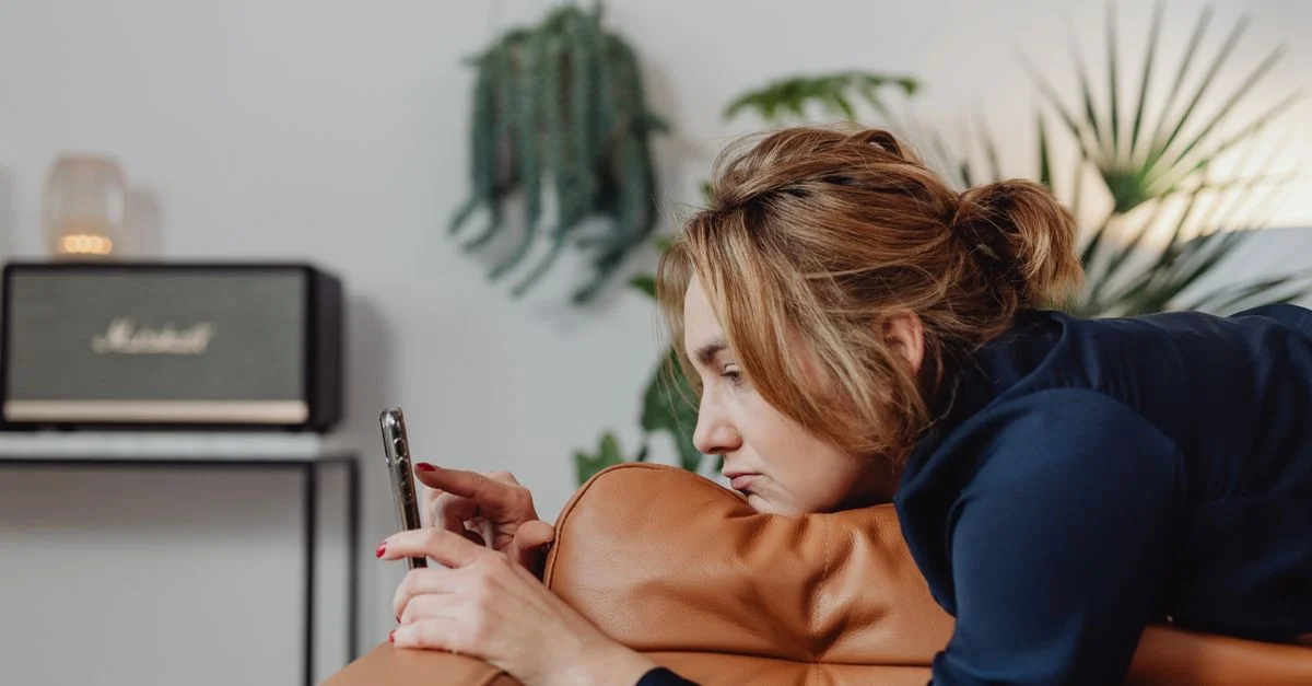 Une femme allongée sur un canapé utilisant son smartphone dans un cadre intérieur confortable.