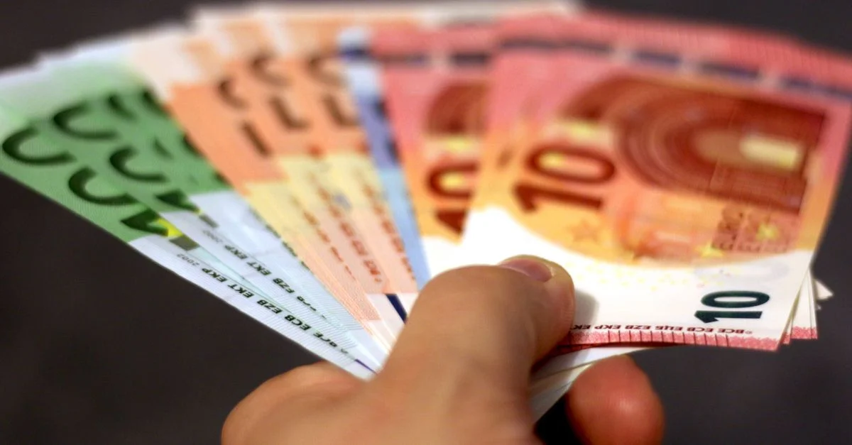 Gros plan d'une main tenant un éventail de billets en euros, symbolisant la richesse et l'échange de devises.
