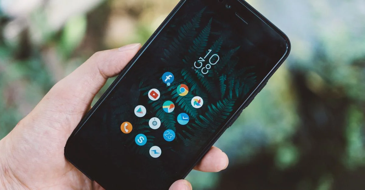 Gros plan sur une main tenant un smartphone avec des icônes d'application et un fond d'écran nature.