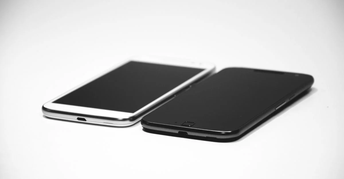 Deux smartphones, un noir et un blanc, placés sur une surface blanche, mettant en valeur un design moderne.